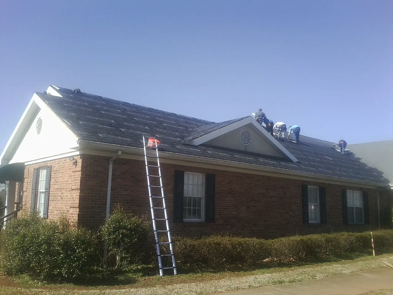 Crew tearing shingles off a brick ranch roof with a ladder set — Emergency Roof Repair work by our crew in Anaheim