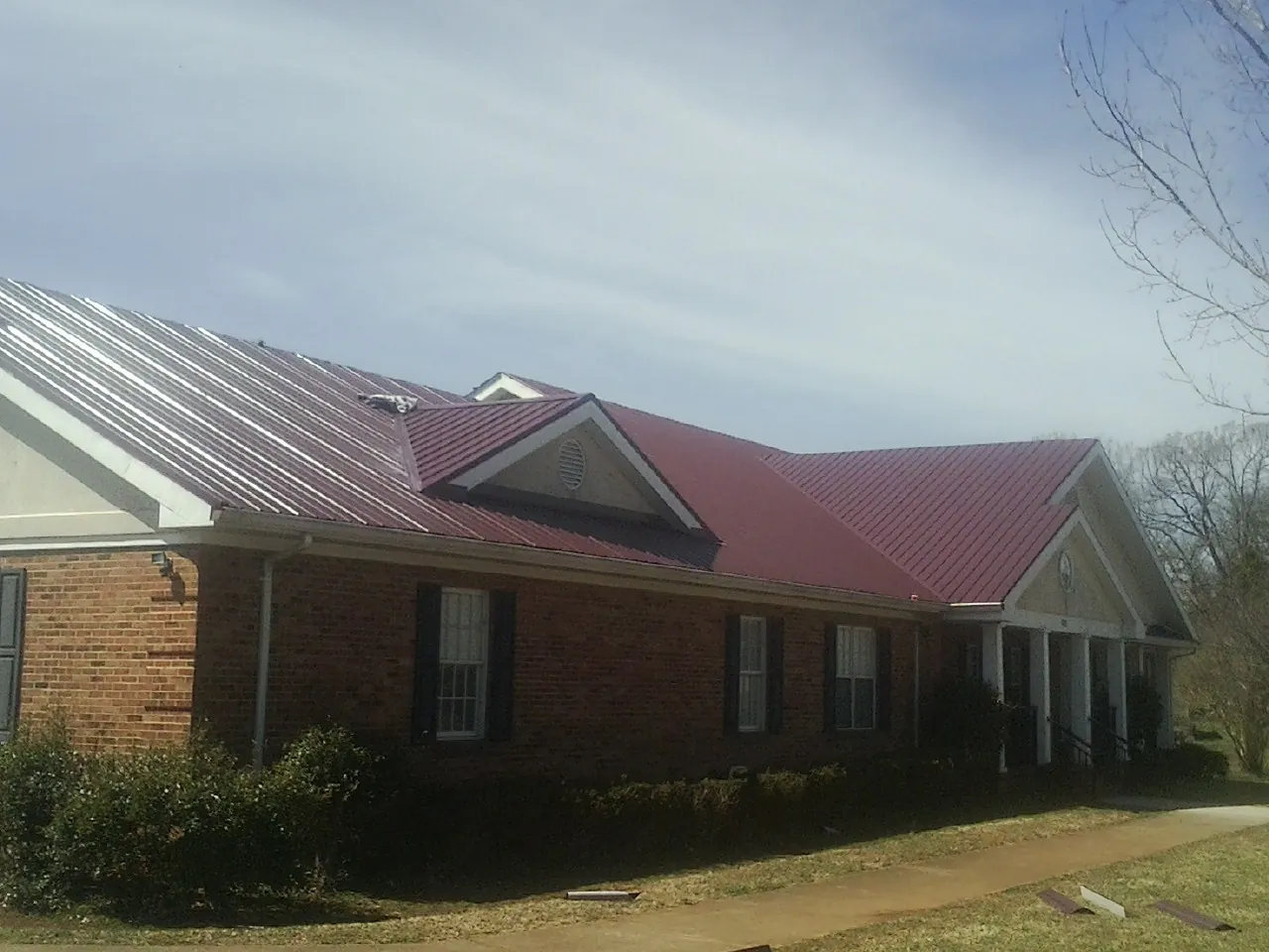 Red metal roof with gabled entries on a long brick building, from a Hail Damage Roof Repair job in Anaheim