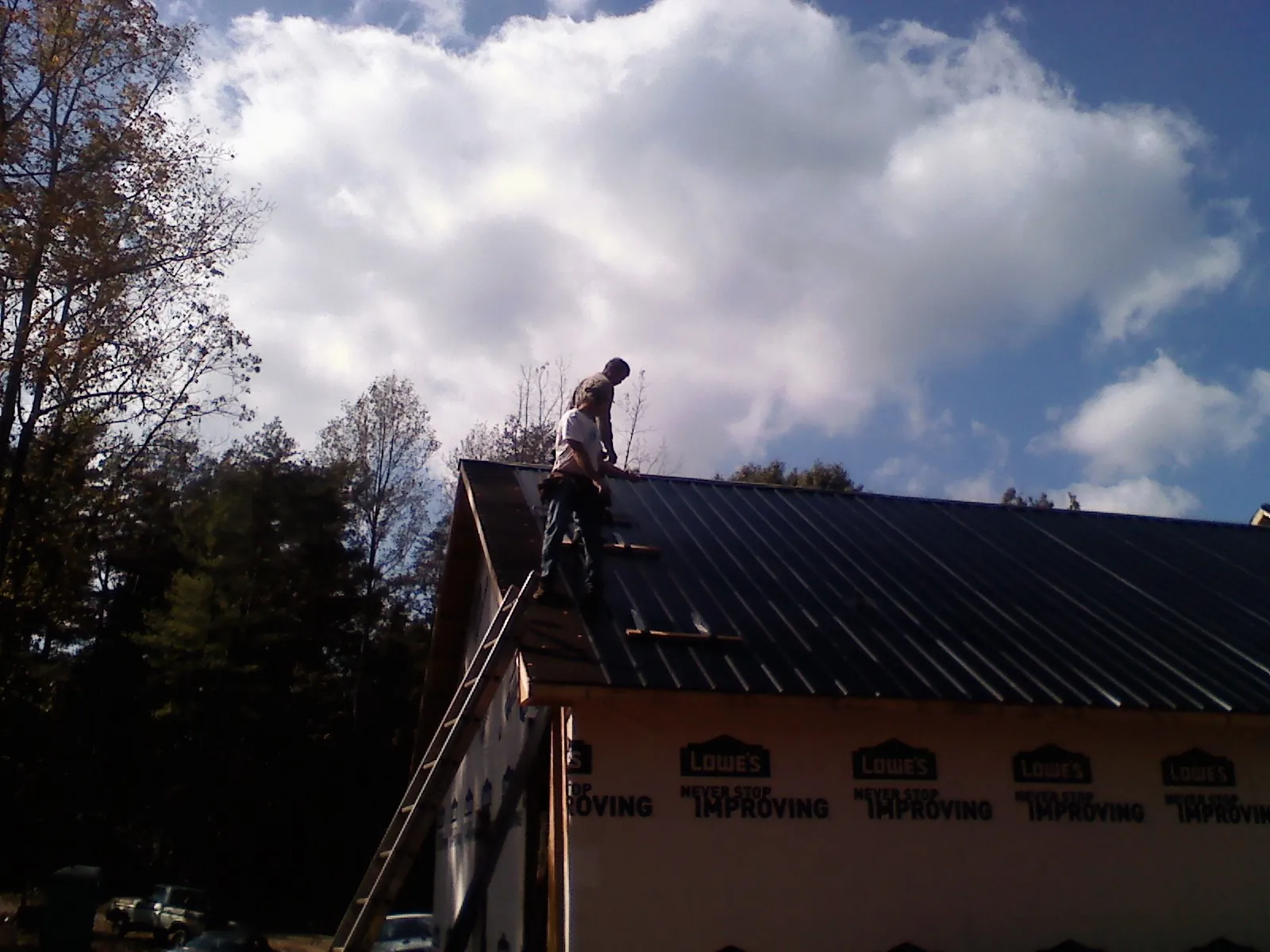 Roofer fastening dark metal panels high against a cloudy sky, from a Roof Inspection job in Anaheim